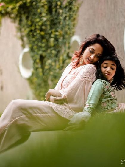 A beautifully composed shot of a mother and daughter cuddling in a serene garden setting. The soft light and lush greenery create a perfect backdrop for this peaceful, loving portrait.