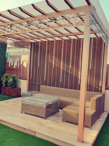 A beautiful pergola with a laser-cut metal canopy and a bamboo-style privacy screen, furnished with comfortable wicker seating.
