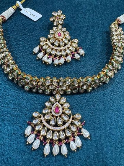 A classic Polki necklace set with a crescent-shaped pendant, detailed with a ruby-coloured stone and pearl drops. This design is timeless and perfect for any traditional celebration, giving a rich and elegant look.