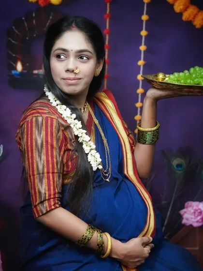 This portrait captures elements of a traditional Dohale Jevan or baby shower ceremony. The gajra in her hair, the plate of fruit, and the festive background celebrate this important milestone.