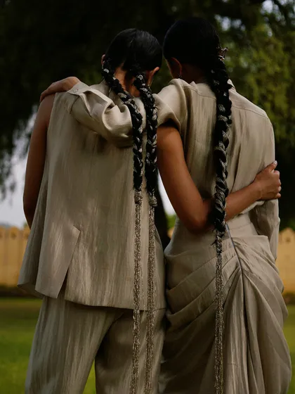 A tender moment between two models, showcasing the back of their outfits and their matching braided hairstyles.