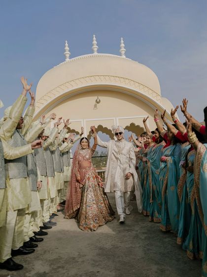 The couple makes a grand, joyous exit from their ceremony, celebrated by an arch of cheering family and friends on a sunlit palace rooftop.
