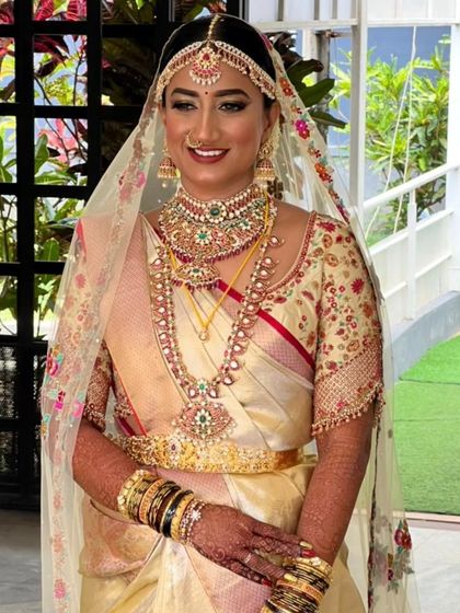 A smiling bride in her custom gold Kanjivaram saree. The blouse features delicate floral embroidery, and the look is completed with a sheer, hand embroidered veil for a touch of modern romance.