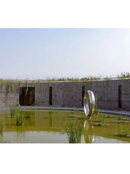 A close-up of the bio-pond within the sunken court, with a metallic ring sculpture at its center. The inclusion of water and native plants is a critical part of my biophilic design philosophy.