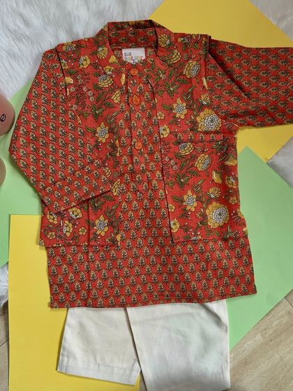 This handcrafted cotton kurta set features beautiful block-printed floral motifs in warm rust and mustard hues. It’s paired with classic white pants for a timeless look.