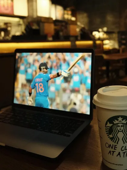 A customer enjoys watching a cricket match on their laptop while sipping a Starbucks coffee, showing how our space is perfect for work, relaxation, and entertainment.