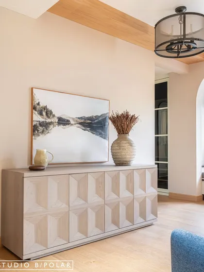 The master bedroom at Sunlit Serenity features a stunning carved wooden console table. The light wood and geometric pattern add visual interest and contrast with the room's soft, neutral tones.
