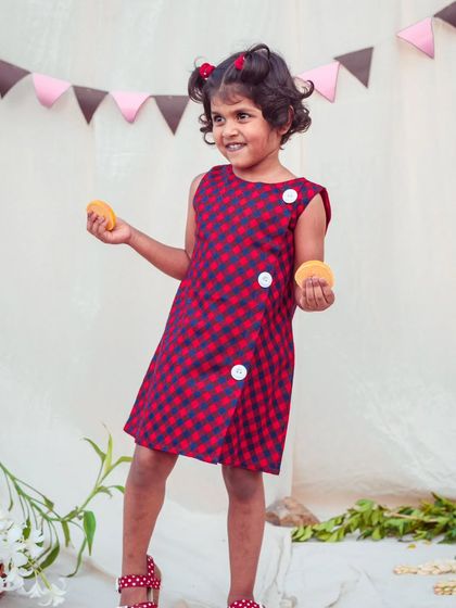 A fun and modern take on a classic checked dress. The wrap-style front with large buttons gives this red and blue gingham dress a unique and playful twist.