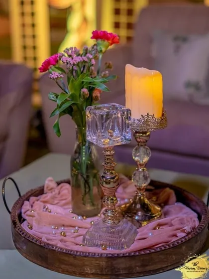 A romantic tabletop detail featuring elegant crystal candle holders and a small vase of pink flowers on a soft, draped tray. These touches add to the overall ambiance of elegance.