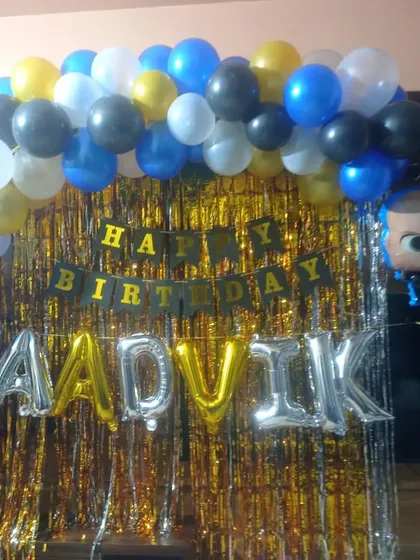A simple Boss Baby themed decoration for a home party. The setup includes a shimmer curtain backdrop, a balloon garland, and a character foil balloon.