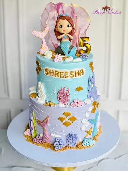Diving into a sea of sweetness with this two-tier mermaid-themed cake, complete with a handcrafted mermaid topper and coral details.