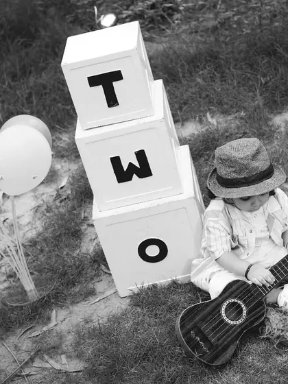 A black and white photo of a two-year-old boy playing a small guitar during his outdoor session. We encourage play to bring out natural expressions.