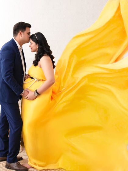 A dramatic and artistic portrait using a flowing yellow fabric. The husband kisses his wife's forehead as the fabric billows around them, creating a sense of movement and magic.