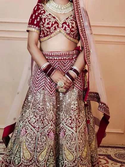 A full view of a bride wearing a maroon and gold lehenga. This shows the complete rental outfit, including the lehenga, choli, dupatta, and jewellery.