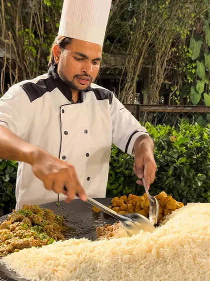 A focused shot of the chef preparing Mutton Tawa Pulao, ensuring every grain of rice is perfectly coated in the savory masala.