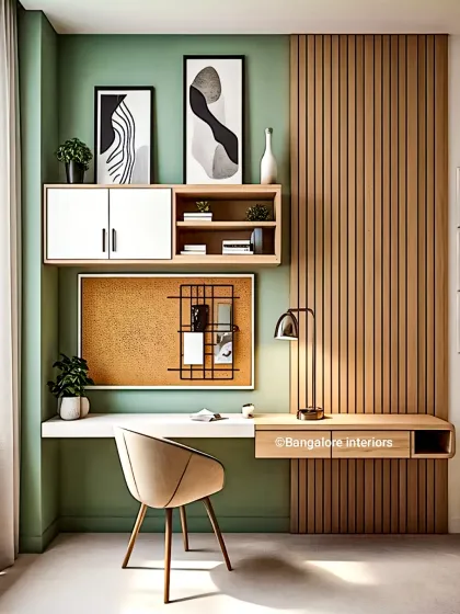 A stylish home office corner featuring a floating desk against a sage green wall. The design includes a corkboard for notes, overhead cabinets, and a textured wood accent panel.