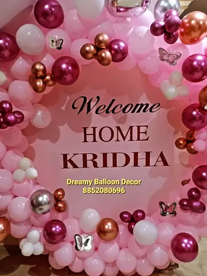 A personalized 'Welcome Home' balloon ring for baby Kridha. The pink, white, and chrome balloon arrangement is decorated with small butterfly accents for a delicate touch.