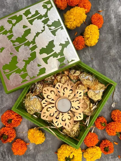 I love the simple elegance of this Diwali gift. A beautiful green and silver box holds a collection of rich, gold-wrapped chocolates and a handcrafted floral diya, making it a perfect token of festive joy for friends or colleagues.