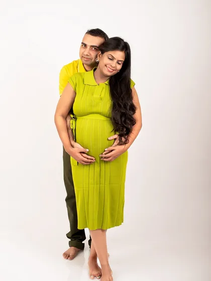 A full-length studio portrait of an expecting couple. The coordinated green and yellow outfits create a harmonious and visually pleasing image.