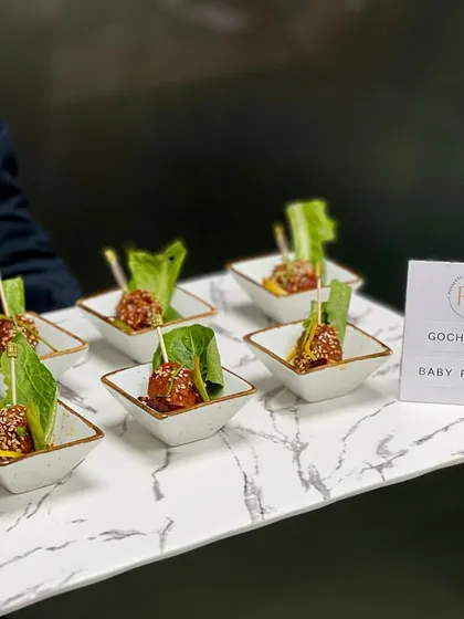 A close-up of our Gochujang Baby Potatoes. These Korean-inspired bites are tossed in a spicy and savory sauce, garnished with sesame seeds, and served in individual ceramic dishes.