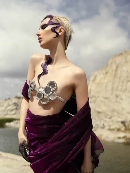 The 'Siren' look captured in bright daylight, showing the details of the purple hair sculpture and the intense, dark eyeshadow.