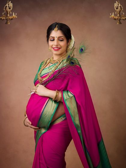 A close-up portrait highlighting the beautiful details of the traditional jewelry and the serene expression of the mother-to-be. The peacock feather adds a touch of divine symbolism.