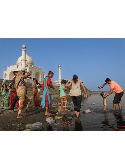 Local families bathe and wash clothes in the river behind the Taj Mahal, a depiction of everyday life that tourists rarely see.