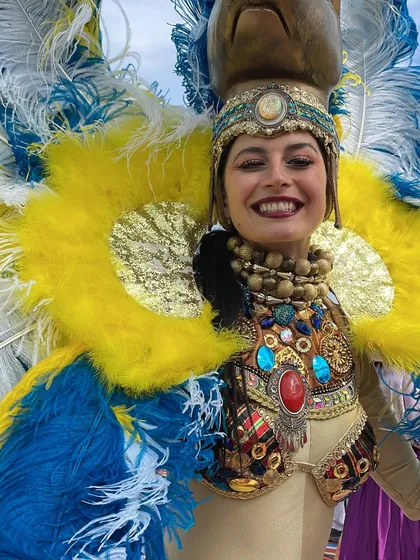 A close-up of a performer in a spectacular blue and yellow feathered costume, embodying the vibrant and celebratory spirit of the carnival theme.