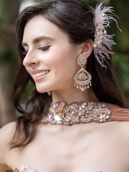 A side view of the soft and natural makeup look. The feathered hair accessory and delicate jewelry add to the ethereal and romantic feel of this style.