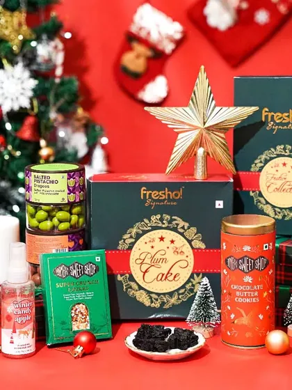 A festive Christmas hamper from Fresho! Signature, beautifully arranged with a plum cake, cookies, and other goodies in front of a Christmas tree. This shot is perfect for a holiday gift catalog.