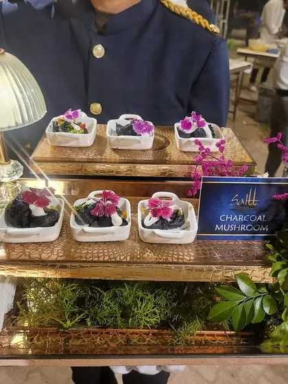 A visually striking appetizer of Charcoal Mushroom, presented in individual white dishes. The dark colour of the mushroom contrasts beautifully with the creamy topping and floral garnish.