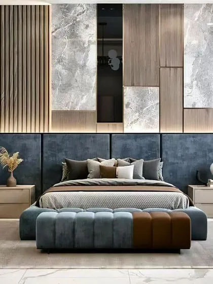 A luxurious master bedroom showcasing a sophisticated mix of textures, including a plush blue upholstered headboard, vertical wood fluting, and marble-patterned wall panels. The ambient backlighting and dedicated shelving create a serene and opulent atmosphere perfect for relaxation.