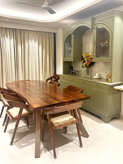 The dining area is anchored by a custom live-edge wooden table, providing an organic contrast to the sophisticated, muted green crockery unit. This space was designed for both family meals and elegant entertaining, balancing functionality with refined aesthetics.