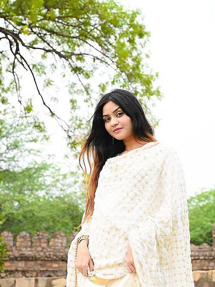 A full shot of the model in a white suit, looking graceful and serene in a natural setting.