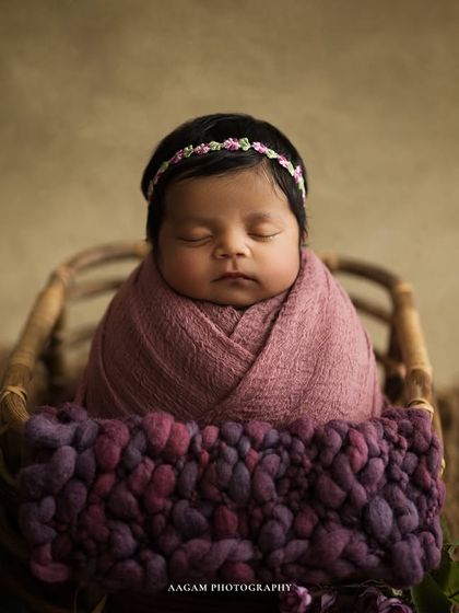 A pop of color with this beautiful mauve wrap. The baby is sleeping peacefully in a basket, adorned with a delicate floral headband and surrounded by purple flowers.