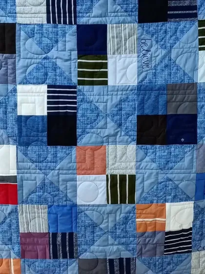 A close-up of the quilted words "Love," "Believe," and "Compassion" on the blue t-shirt quilt.