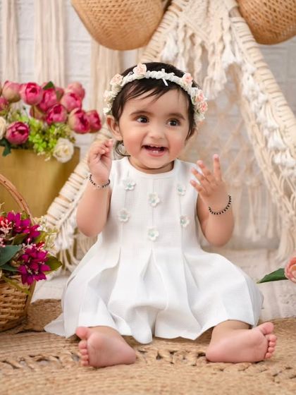 A happy baby girl surrounded by pink and white florals in a boho setting. The natural textures of the rug and baskets add a rustic touch.