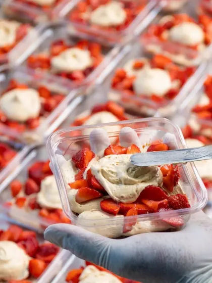 A close-up of our Strawberry Pistachio dessert tubs being prepared. Each tub is carefully layered with cream, fresh strawberries, and a dollop of pistachio cream.