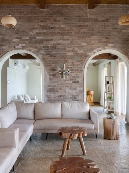 The living room of the 'Ekaant' villa, showing the harmony between the rough texture of the brick wall and the smooth finish of the neutral-toned sofa.