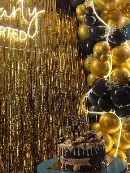 The birthday cake is ready for its moment in front of the shimmering gold backdrop and custom balloon arrangement.