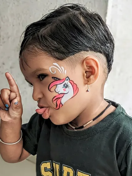 A cheeky toddler with a unicorn face paint, showing that you're never too young to enjoy a bit of color.