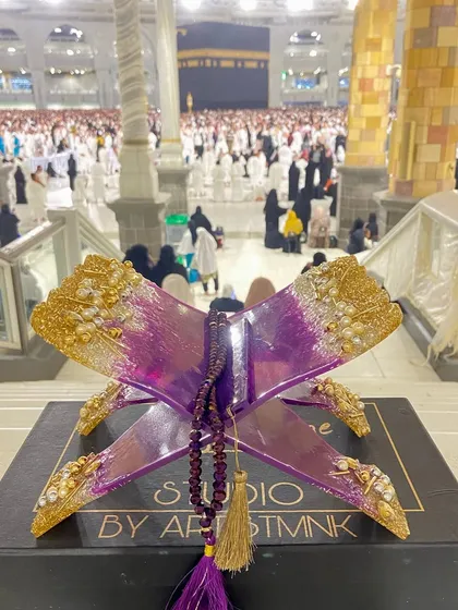 This striking Quran holder is made with a vibrant purple and gold resin design. It comes with a matching crystal tasbeeh and is shown here at the holy city of Makkah, adding to its spiritual significance.