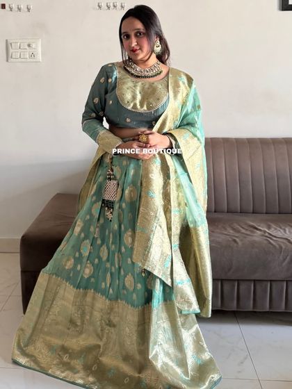 A full-length view of the sage green Banarasi lehenga, complete with a matching dupatta. This is a perfect choice for a wedding guest who wants a sophisticated and classic look.