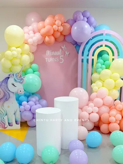 A rainbow and unicorn themed 5th birthday party. This pastel-colored setup includes a unicorn cutout, a rainbow arch prop, and soft-hued balloons.