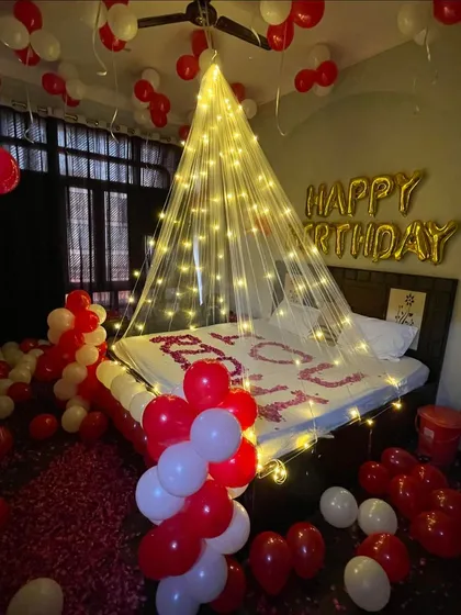 This is my classic romantic birthday decoration, perfect for surprising your partner. I use a canopy of fairy lights to create a dreamy focal point over the bed, complemented by hundreds of red and white balloons and rose petals on the bed and floor.
