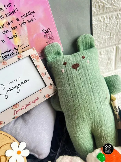 A close-up of the sonogram frame and a soft green teddy bear from a newborn gift hamper. It's a beautiful way to commemorate the 'love at first sight' moment.