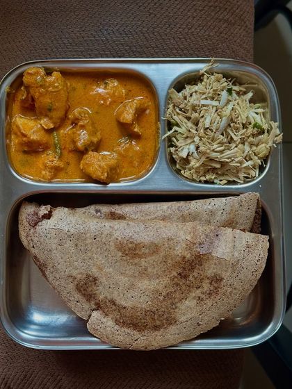 A unique combination of ragi dosa with chicken curry and a side of cabbage palya.