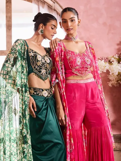Two models showcasing vibrant festive wear. The makeup for both is kept cohesive with an emphasis on defined eyes and a warm, peachy blush that complements both the pink and green outfits.