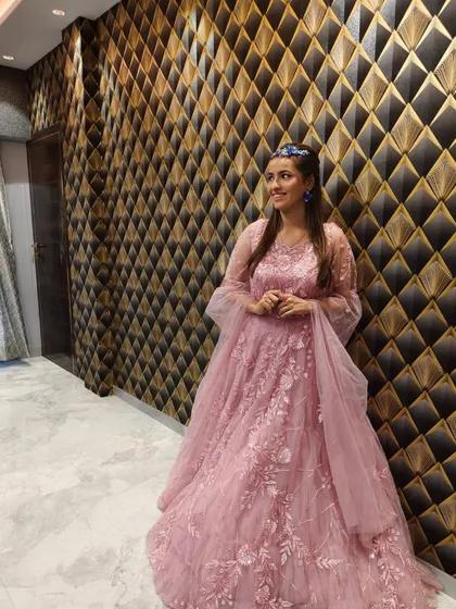 A client posing in a beautiful dusty pink gown with floral embroidery and bell sleeves.