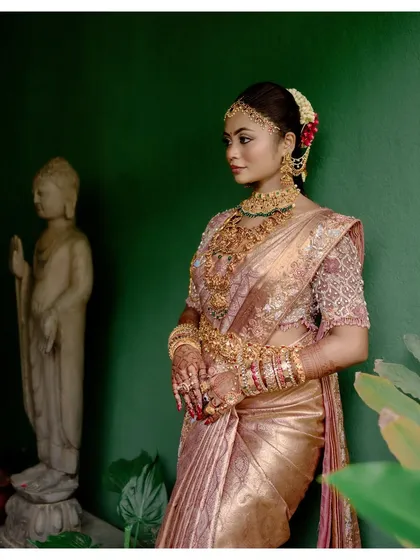 A bride, adorned in gold, stands next to a Buddha statue, a portrait that is both regal and serene.